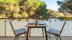 A balcony with a table set for two, two cushioned chairs, and a view of trees and buildings. - Charming apartment in La Fosca - 4 guests (Palamós)