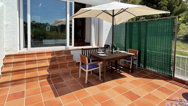 Un patio con tavolo e sedie, un ombrellone grande e un recinto verde.