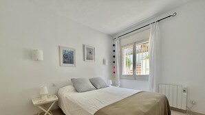 Une chambre à coucher avec un lit, une table de chevet avec une lampe, un radiateur et une fenêtre avec des rideaux.