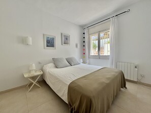 Ein Schlafzimmer mit Bett, Nachttisch mit Lampe, Heizkörper und einem Fenster mit Vorhängen.