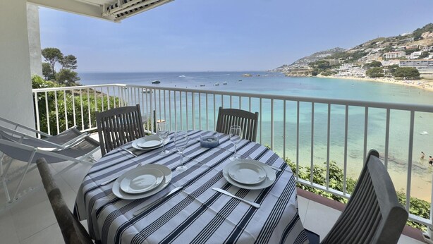Un balcon avec une table dressée pour le dîner, donnant sur une zone côtière où le ciel est dégagé et où l’on peut voir des bateaux sur l’eau.