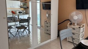 Eine kompakte Küche mit Essbereich, einem an der Wand montierten Fernseher und einem bodenstehenden Ventilator.