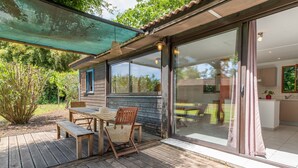 Eine Holzterrasse mit Tisch und Stühlen, eine Glastür, die zum Küchenbereich führt, und eine überdachte Terrasse.
