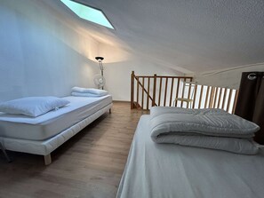 Ein Schlafzimmer mit zwei Betten, einem Oberlicht, einem Ventilator und einem Holzbalken.