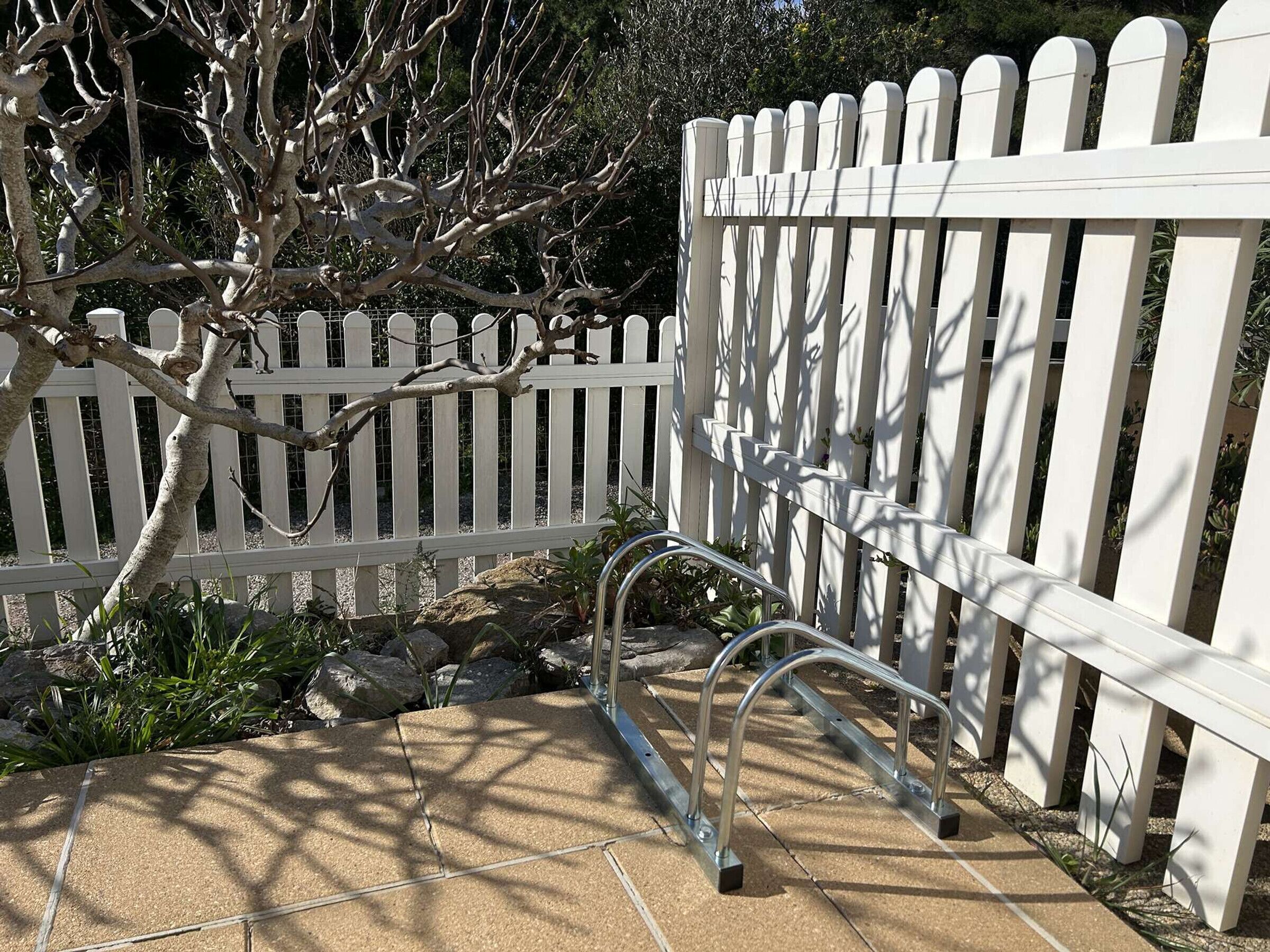 Une clôture blanche en bois avec des barreaux métalliques, un chemin de pierre et un arbre aux branches nues.