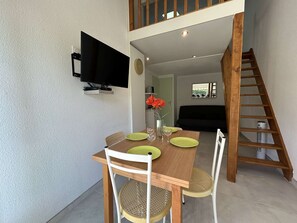 Un comedor con una mesa y sillas de madera, un televisor montado en la pared y una escalera que sube a un nivel superior.