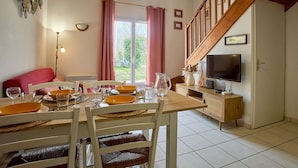 Een eetruimte met een houten tafel voor vier personen, een televisie en een trap naar een hoger niveau.