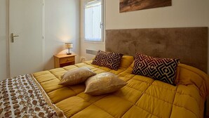 Een slaapkamer met een bed, een nachtkastje, een raam en een aan de muur hangend schilderij.