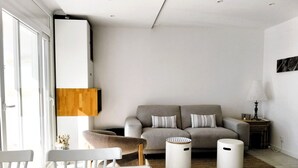 Ein modernes Wohnzimmer mit Sofa, zwei Beistelltischen, einer Lampe und einem Essbereich mit Stühlen und Tisch.