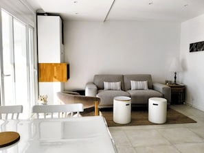 Ein modernes Wohnzimmer mit Sofa, zwei Beistelltischen, einer Lampe und einem Essbereich mit Stühlen und Tisch.