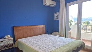 A bedroom with a wooden headboard, a bed with a white and green quilt, a nightstand with candles, and a view of the outdoors through a sliding door. - Charming townhouse near river - 6 guests (Denia)