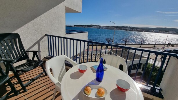 Een balkon met een tafel, stoelen en uitzicht op zee.