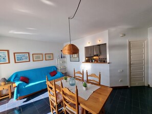 Un salon lumineux avec un canapé bleu, une table à manger en bois et un coin cuisine avec une fenêtre.