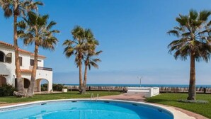 A swimming pool with a clear blue water, surrounded by palm trees and a white building with arches. - Apartment with sea view - 4 guests (Denia)