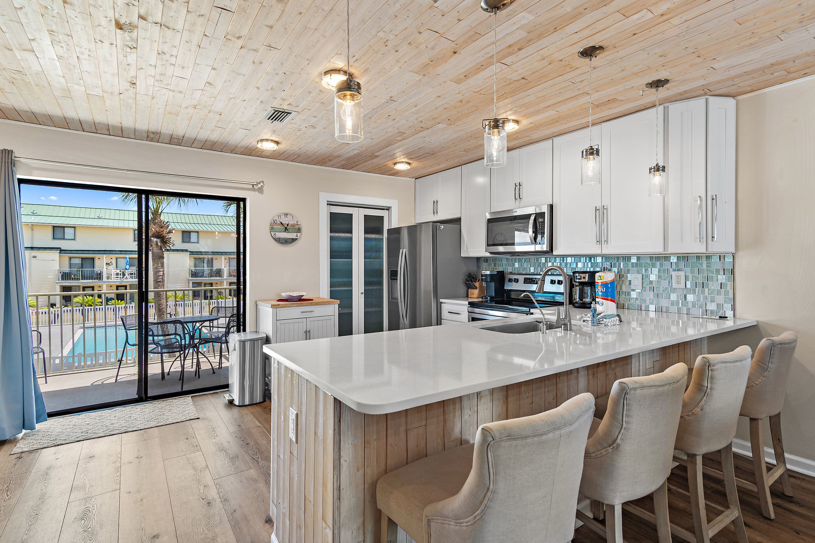A modern kitchen with a large island, stainless steel appliances, and a view of a pool.