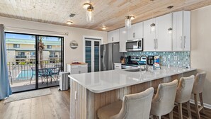 Een moderne keuken met een groot eiland, roestvrijstalen apparatuur en uitzicht op een zwembad.