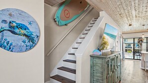 Een trap met houten treden, een aan de muur bevestigd surfboard en een schilderij van een strand.