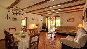 Un área de comedor con una mesa preparada para cuatro, un sofá y un televisor al fondo.
