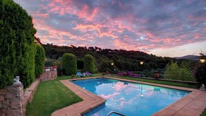 Una piscina con borde de piedra, rodeada de césped y setos bien cuidados.