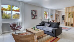 A modern living room with a grey sofa, a wooden coffee table, a wicker chair, and a colorful striped rug. - Large villa for 2 families - 6 bedrooms - Secure swimming pool - Six-Fours (Six fours les plages)