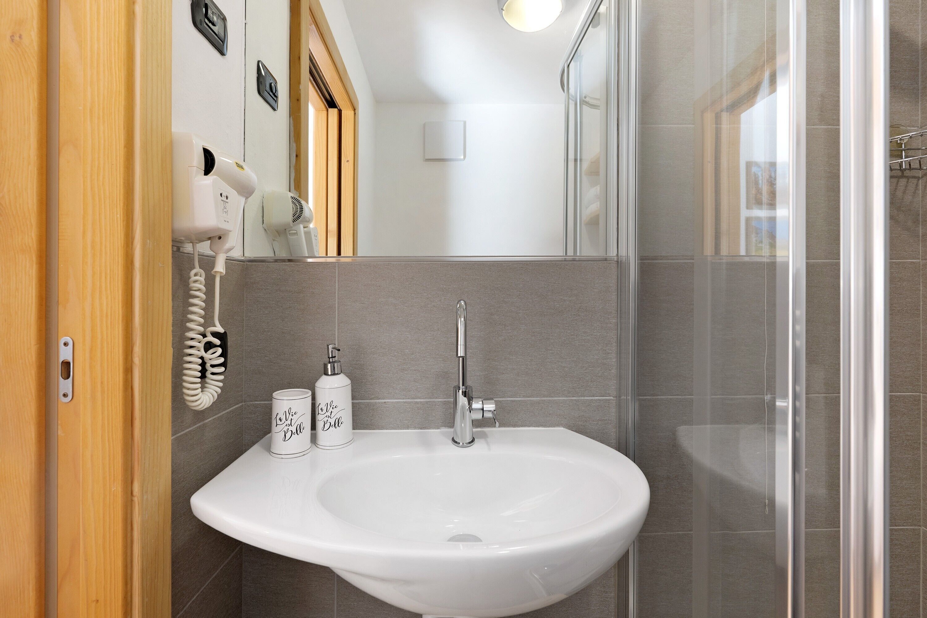 Un baño con lavamanos blanco, secador de pelo y jabón de manos.