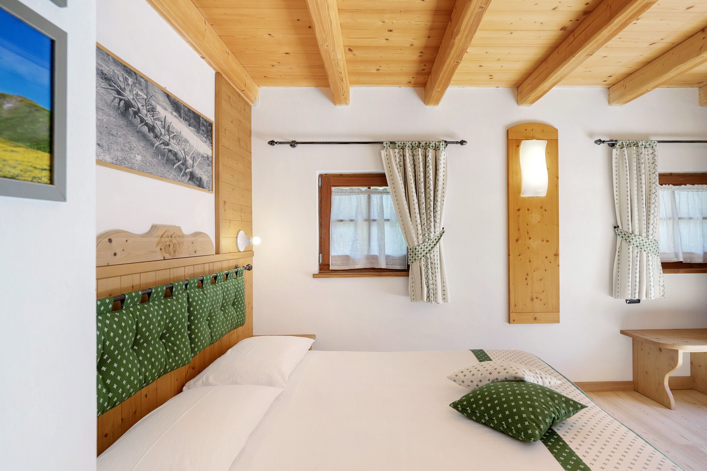A bedroom with a wooden headboard, a bed with white and green bedding, a wooden bench, and a window with curtains.
