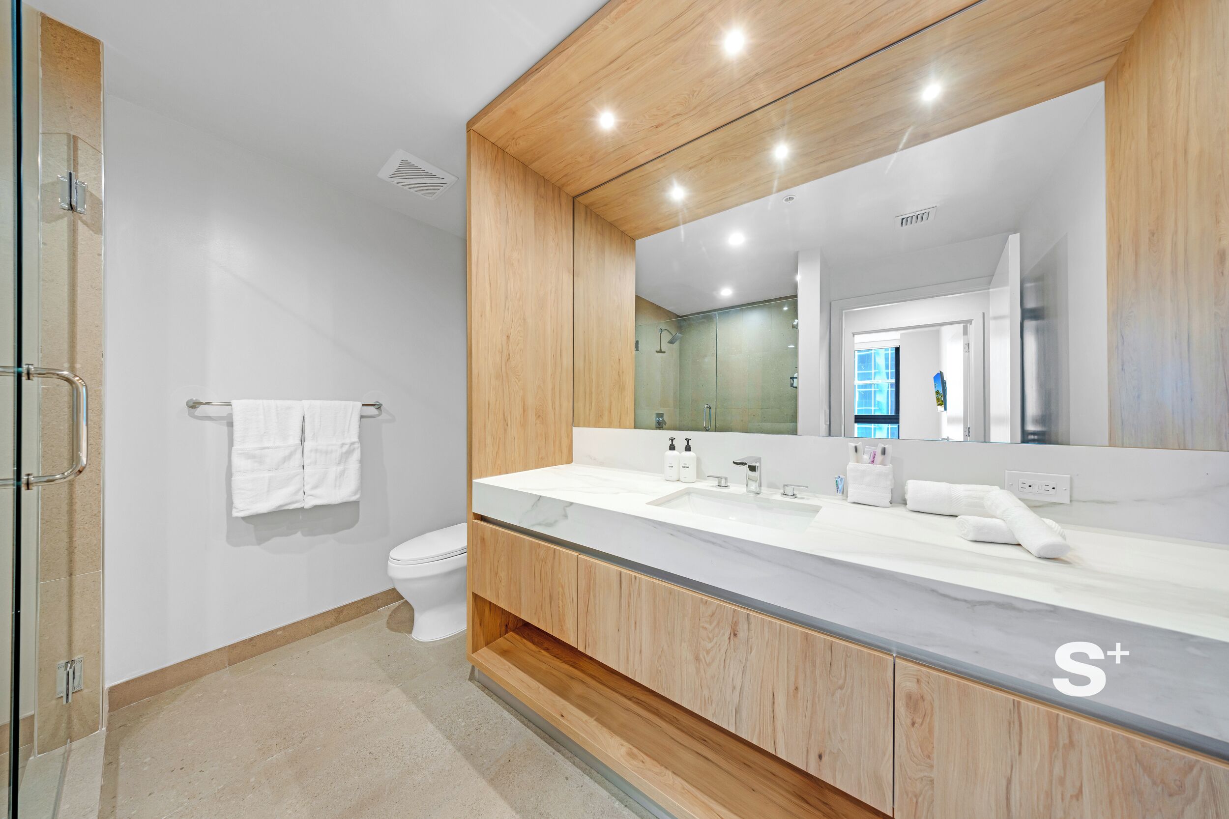 A modern bathroom with a wooden vanity, a large mirror, and a glass shower enclosure.