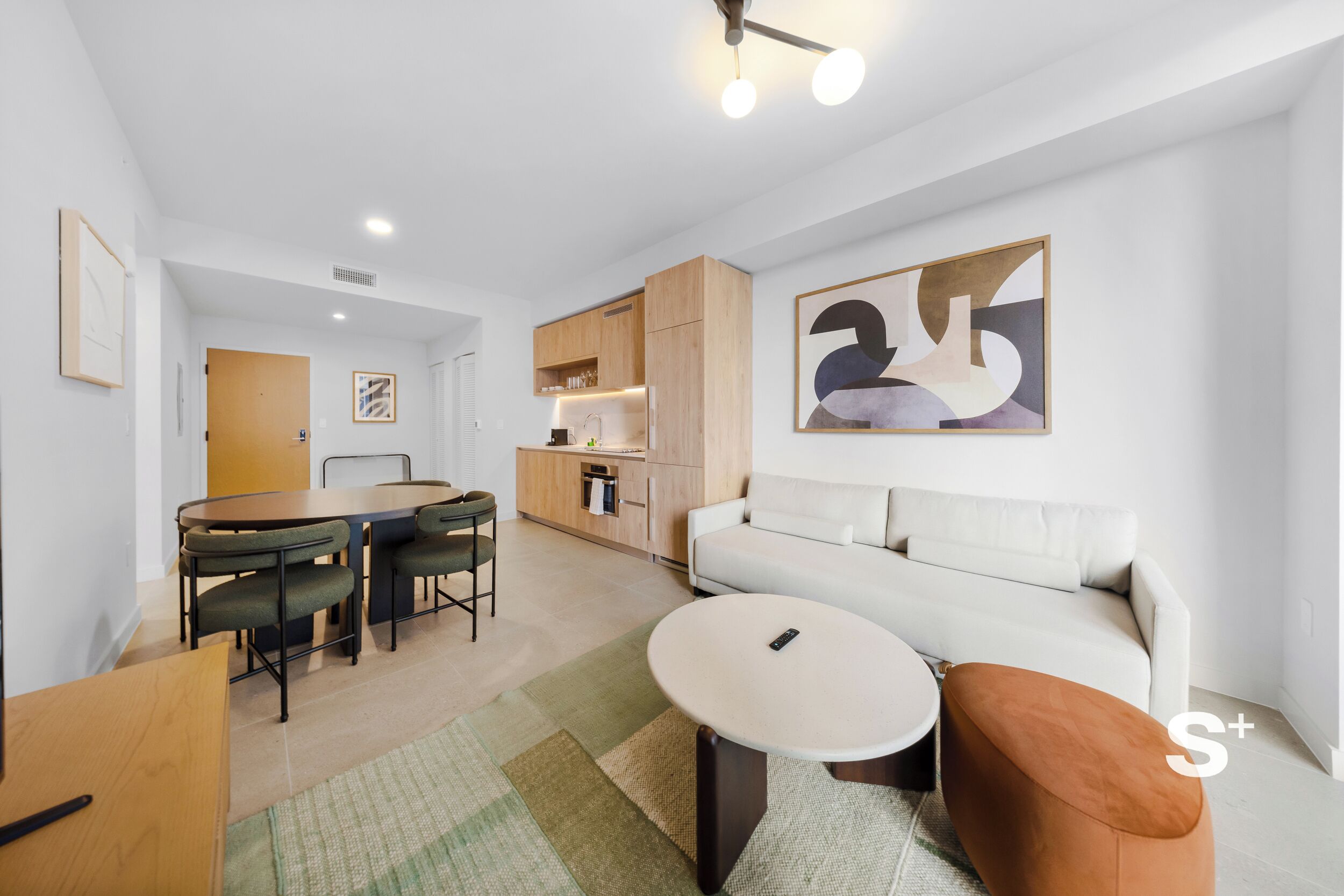 A modern living room with a sofa, a round coffee table, and a dining area with chairs and a table.
