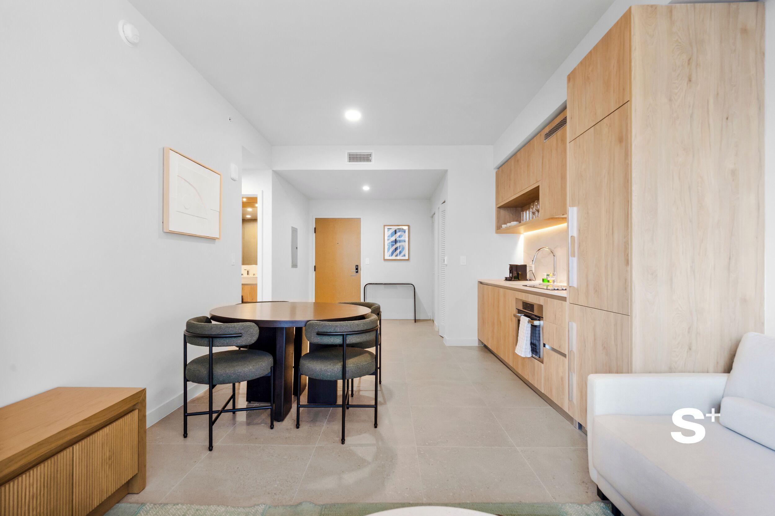 Una cocina moderna con armarios de madera, un área de comedor con una mesa redonda y sillas, y un sofá blanco.