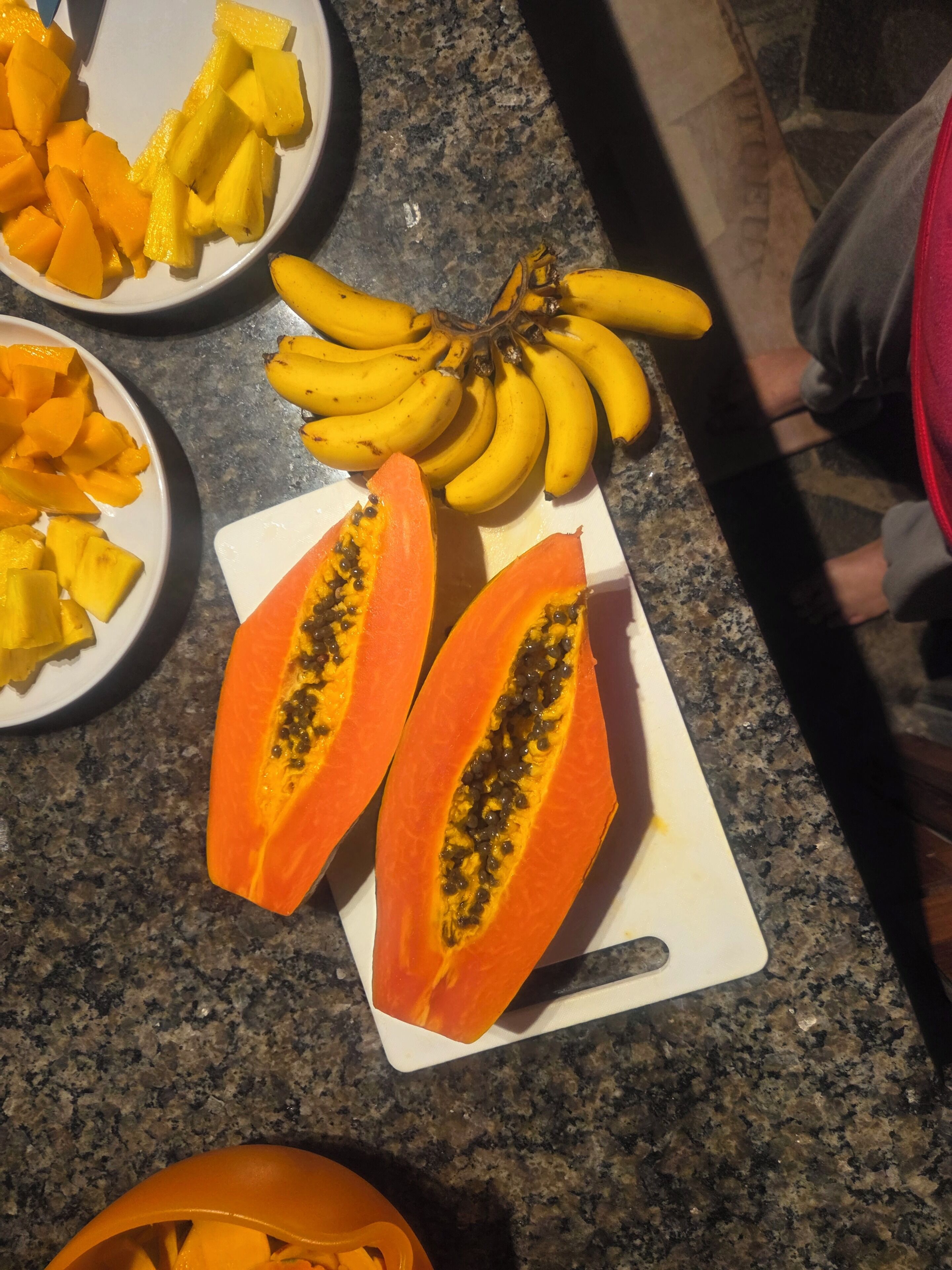Una encimera con un plato de mango en rodajas, un racimo de plátanos y dos mitades de papaya.