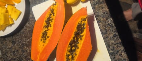 Una encimera con un plato de mango en rodajas, un racimo de plátanos y dos mitades de papaya.