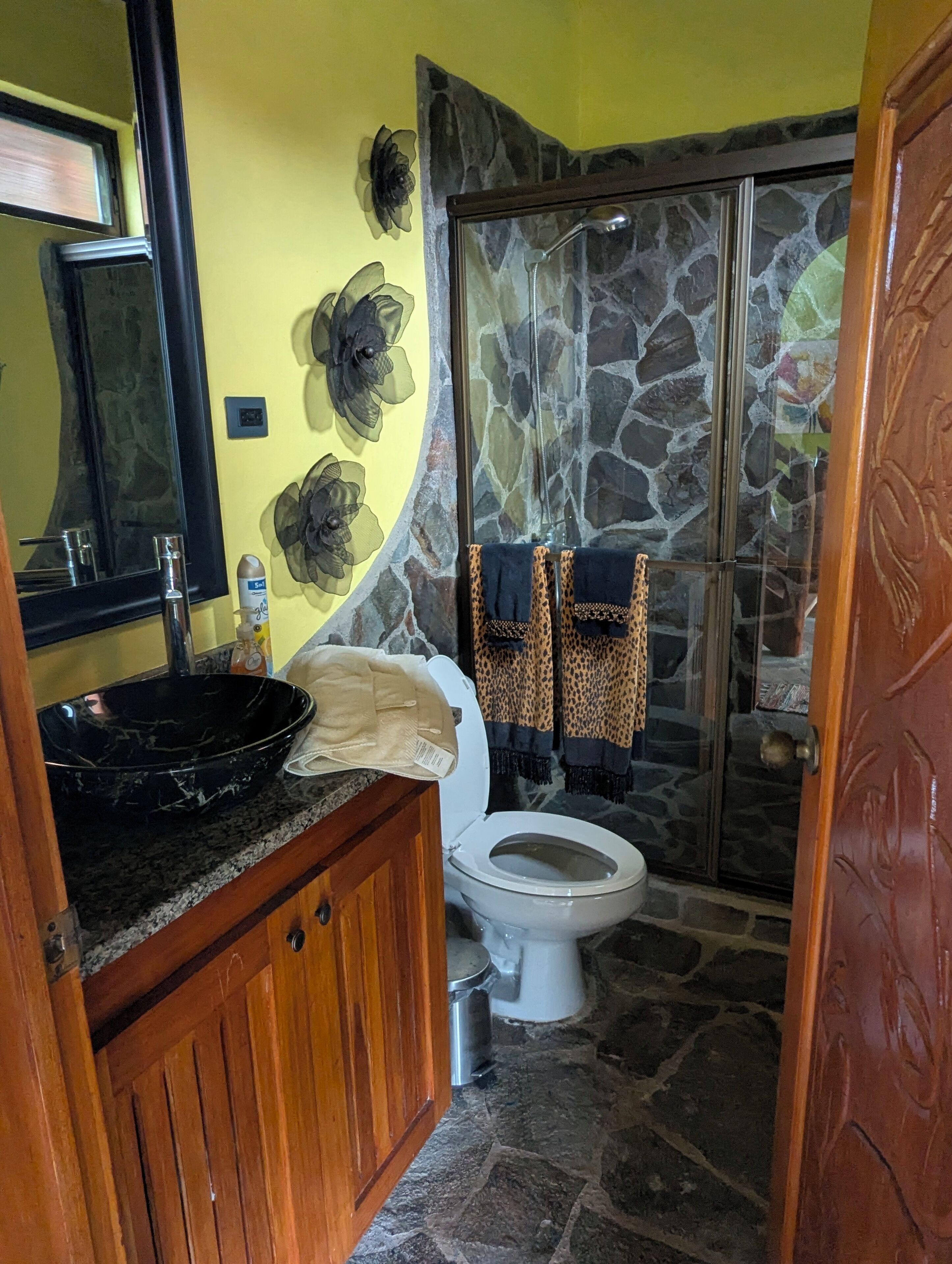 A bathroom with a stone shower, a white toilet, a black sink, and a mirror.