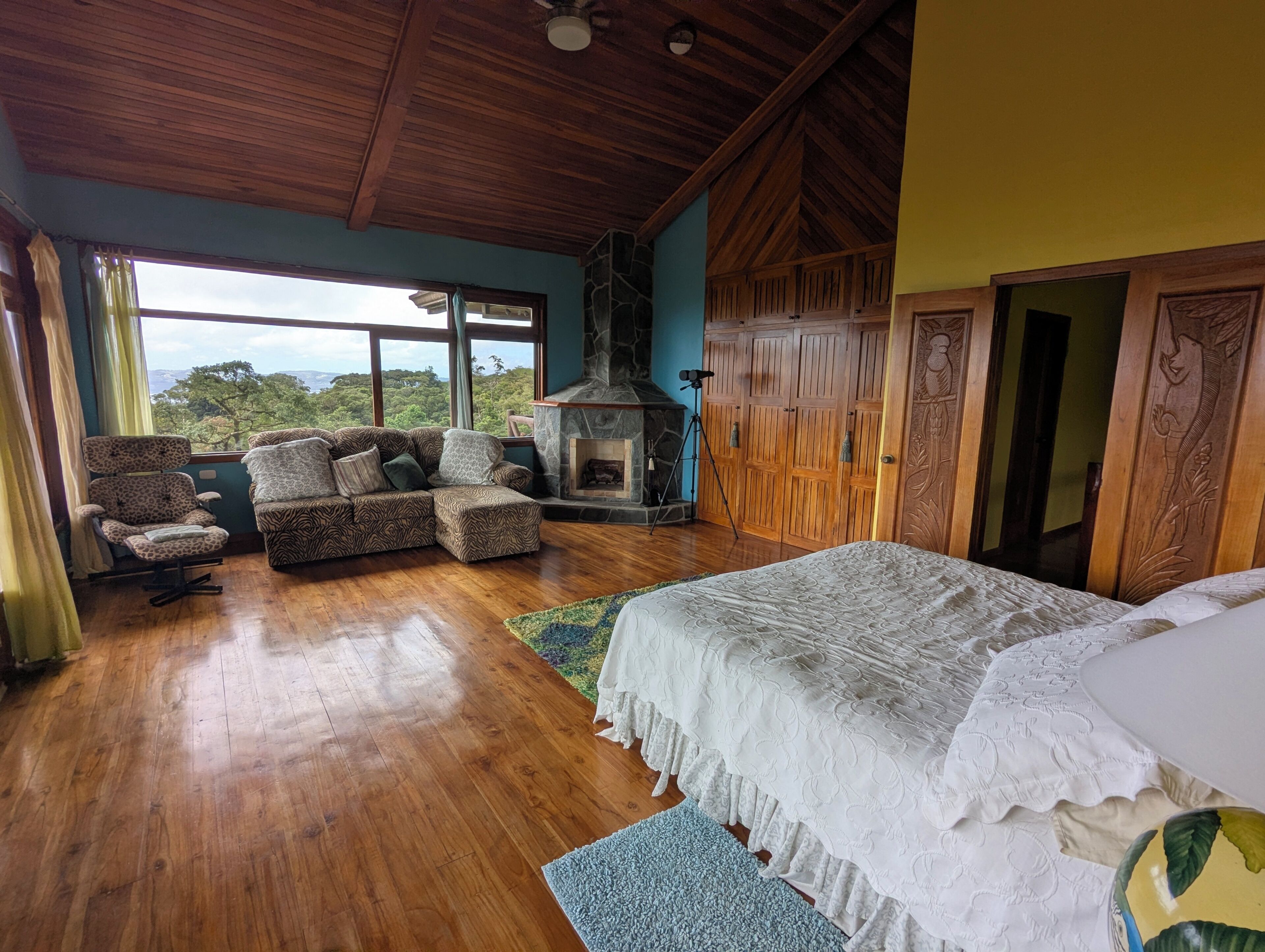 Una habitación amplia con una cama grande, un sofá, una silla, una chimenea y vistas al exterior.