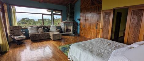 Una habitación amplia con una cama grande, un sofá, una silla, una chimenea y vistas al exterior.