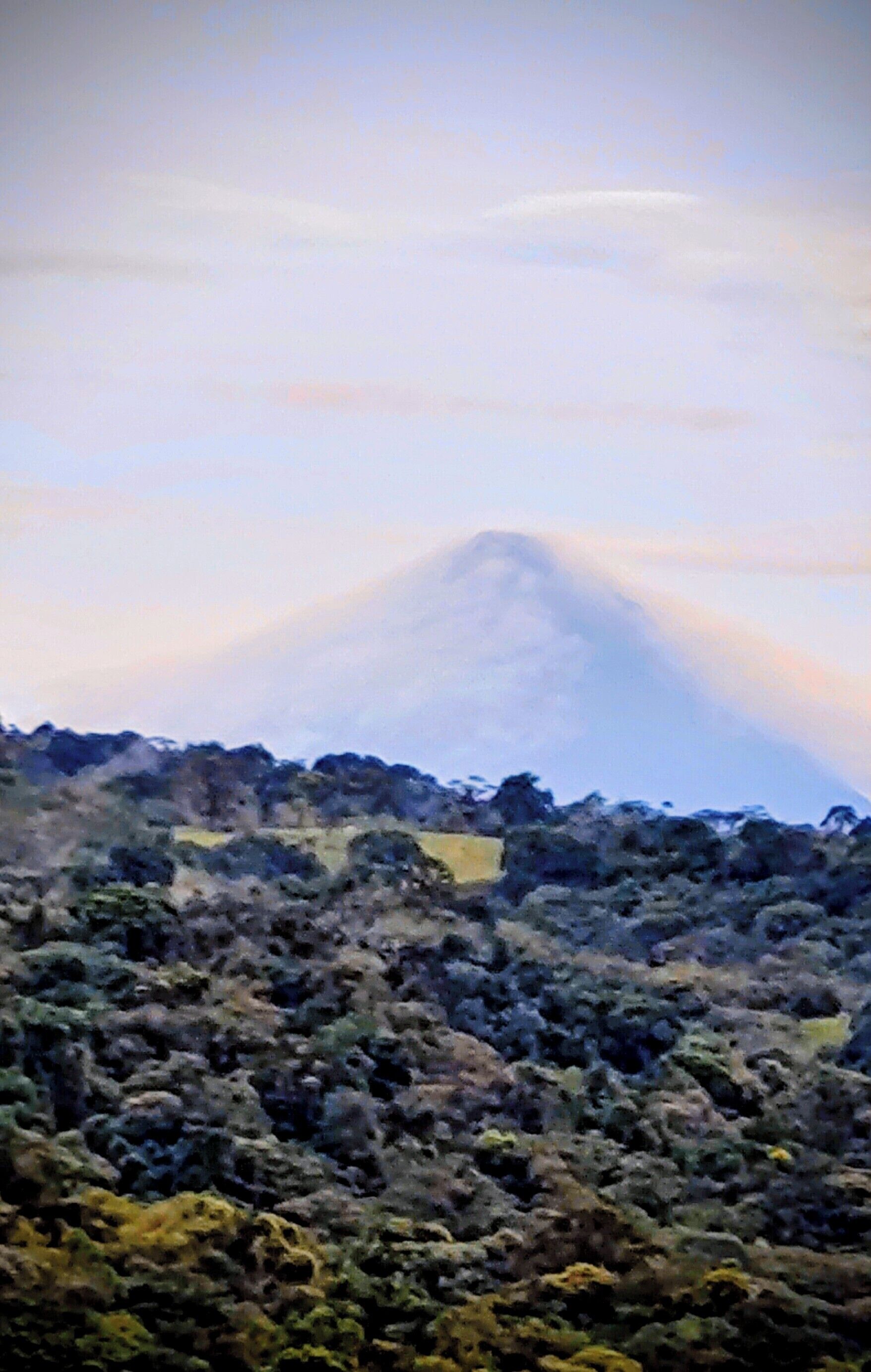 Un paisaje montañoso con un pico destacado y un valle de vegetación densa.