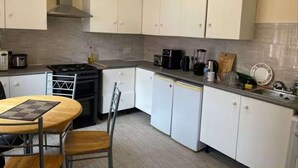 A compact kitchen with white cabinets, a gas stove, a sink, and a dining area with a table and chairs. - 1-bed Apt, Sleeps 4, Old Trafford Nearby (Manchester)