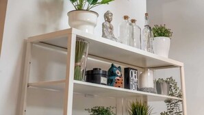 Een witte plank met diverse decoratieve objecten, waaronder planten, een Boeddhabeeld en glazen flessen.