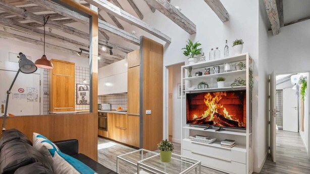 Een moderne woonkamer met een open haard, houten kasten en een keuken op de achtergrond.