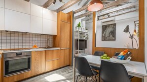 Een moderne keuken met houten kastjes, een inbouwoven en een eethoek met een witte tafel en zwarte stoelen.