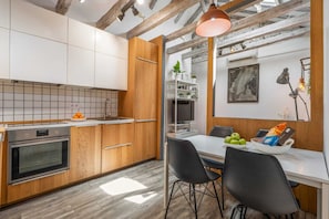 A modern kitchen with wooden cabinets, a built-in oven, and a dining area with a white table and black chairs. - Attic 3 bedroom, 2 baths in heart of Malasana for extended stays (Madrid)