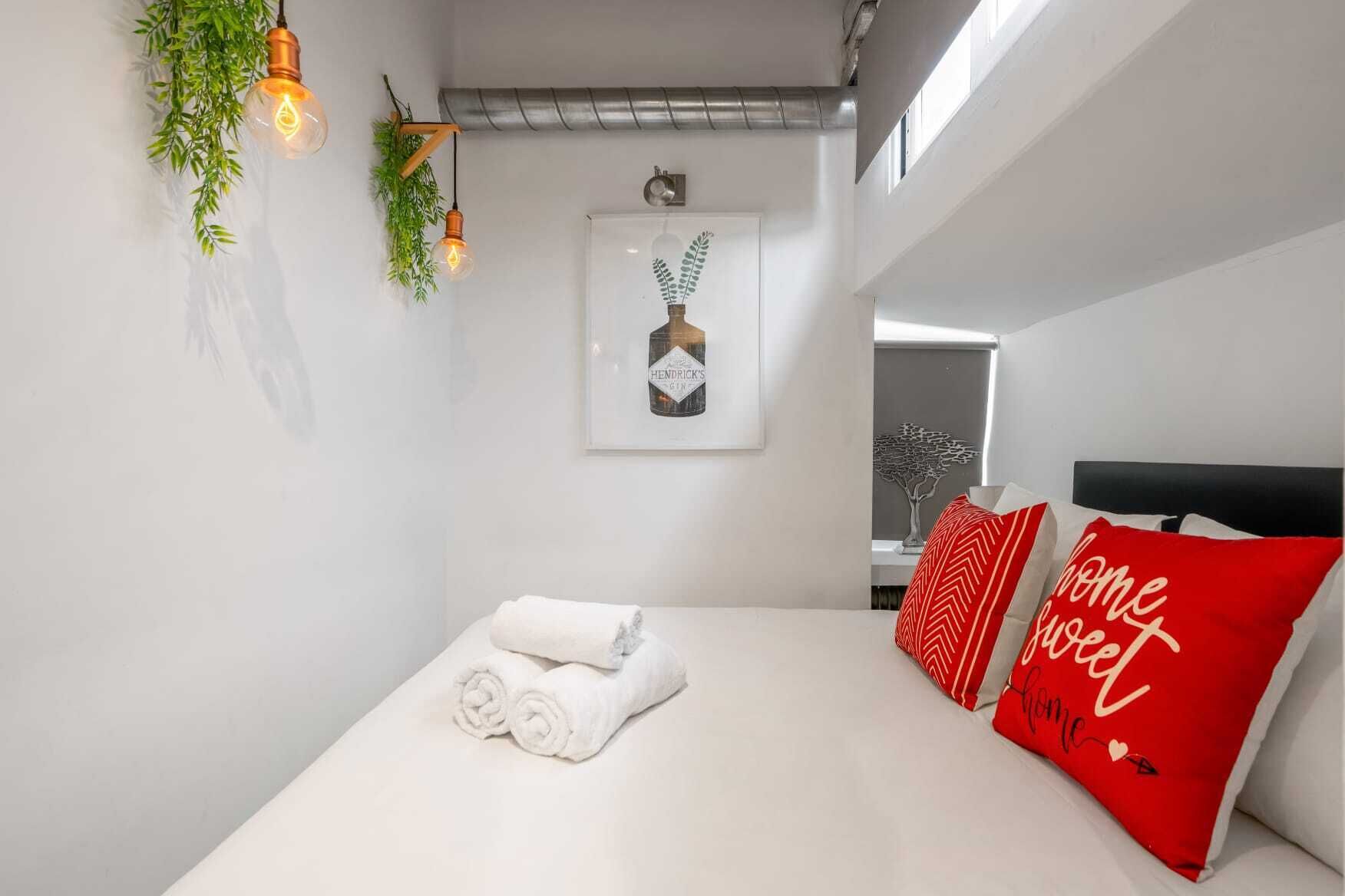 Une chambre à coucher moderne, avec un lit soigneusement fait, une œuvre d’art encadrée au-dessus, et une fenêtre donnant sur un arbre.