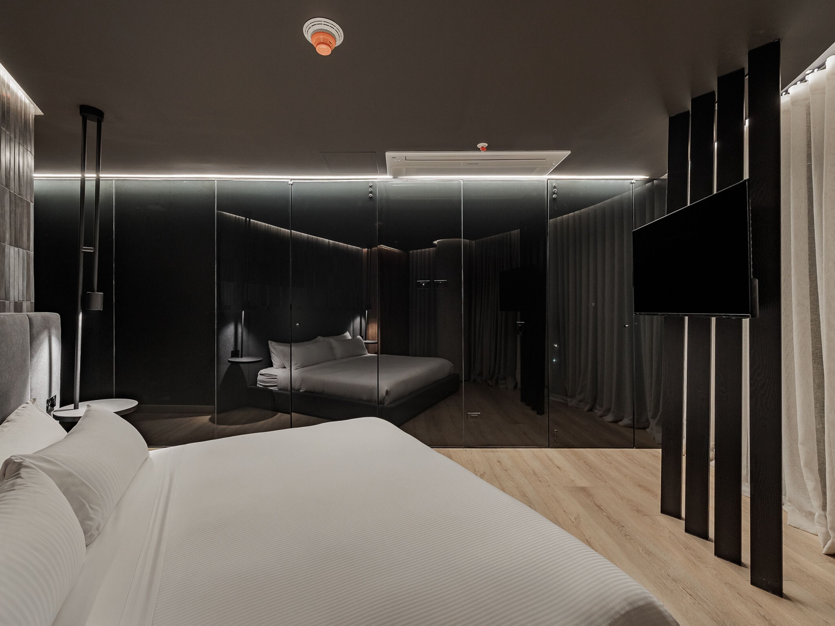 A modern bedroom with a large bed, a flat-screen TV, and a mirror wall.