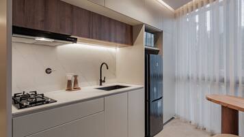 Una cocina moderna con estufa a gas integrada, refrigerador de acero inoxidable y un gabinete de madera sobre el lavamanos.
