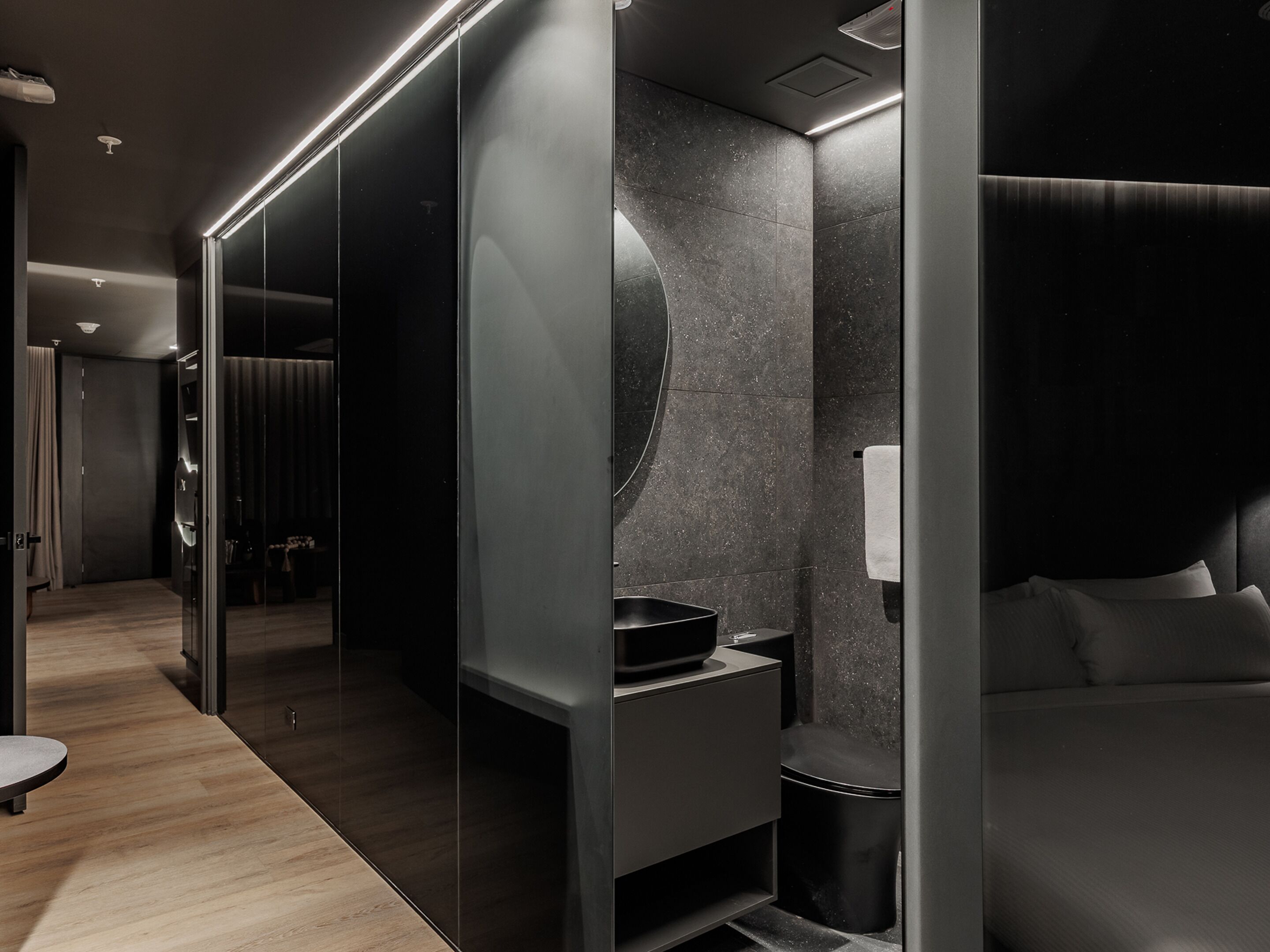 A modern, dark-themed hotel room with a large bed, a built-in vanity, and a mirror.
