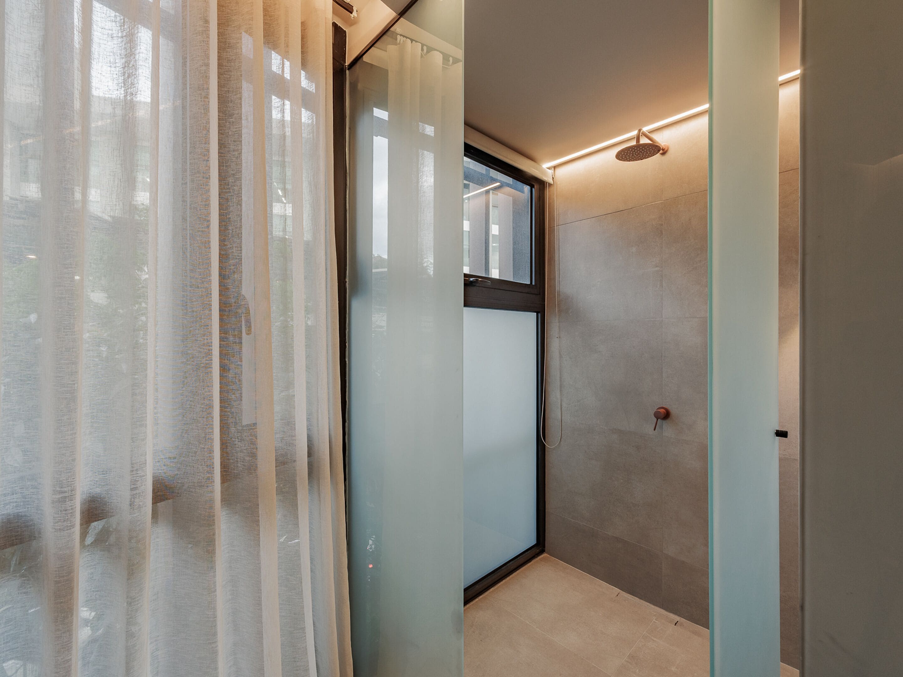 A modern bathroom with a glass shower enclosure, frosted glass doors, and a visible window.