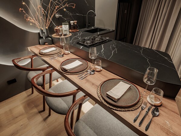 A modern dining area with a long wooden table set for four, equipped with woven placemats, folded napkins, and cutlery. - Devú (Medellín)