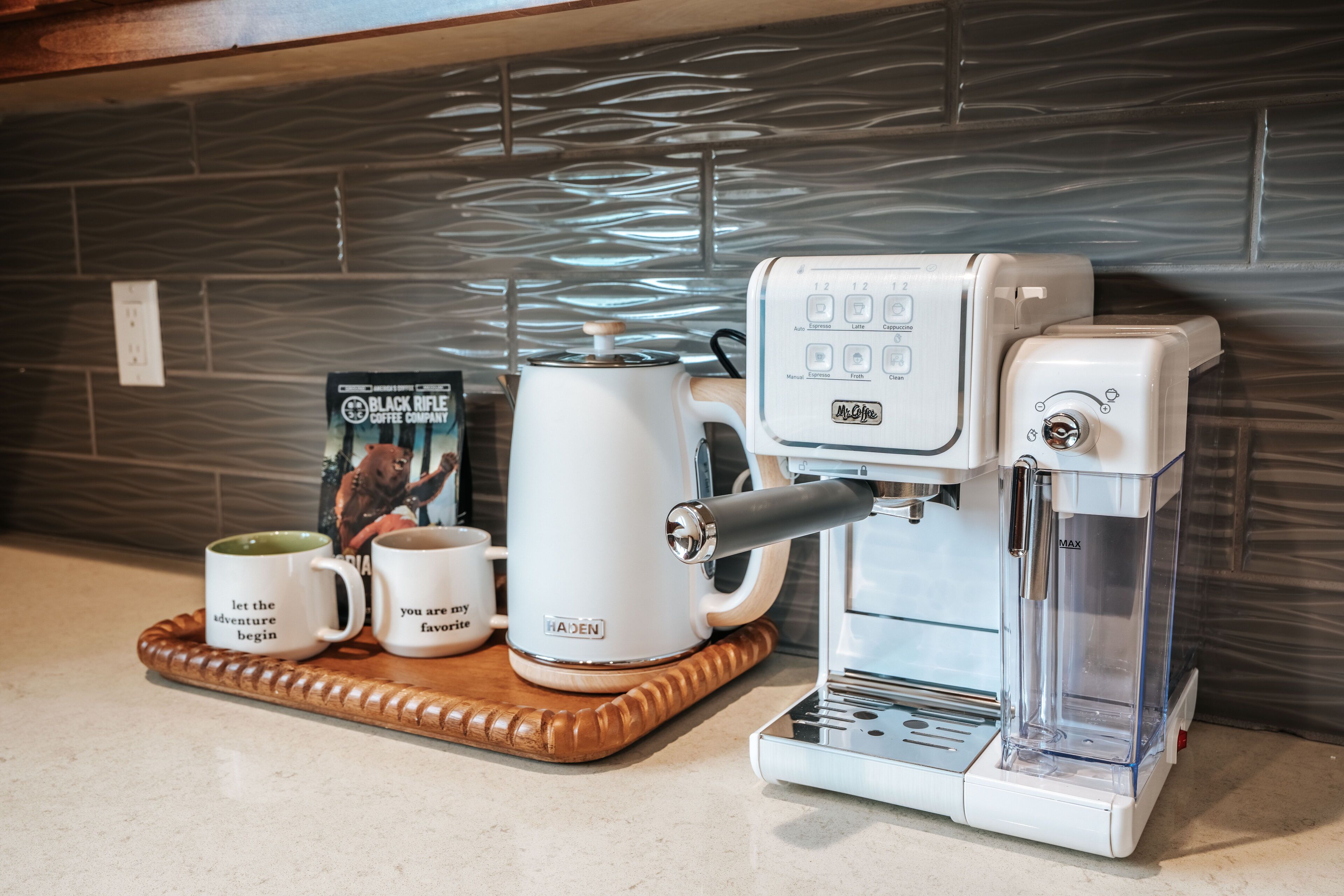 Une machine à café avec un réservoir d’eau, une verseuse et deux tasses sur un plateau.