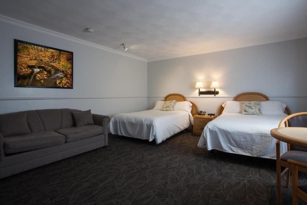 A hotel room with two beds, a sofa, a small table, and a painting on the wall.