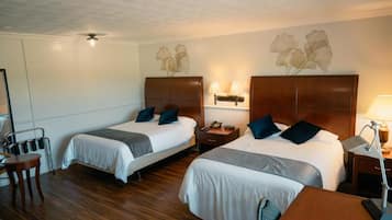 Habitación de hotel con dos camas, cabeceros de madera, mesitas de noche con lámparas, una pequeña mesa redonda y una silla.