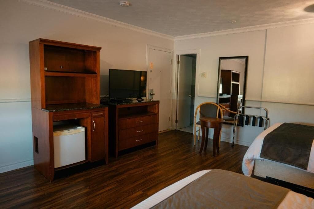Una habitación de hotel con un escritorio de madera, televisión, una silla y una cama.